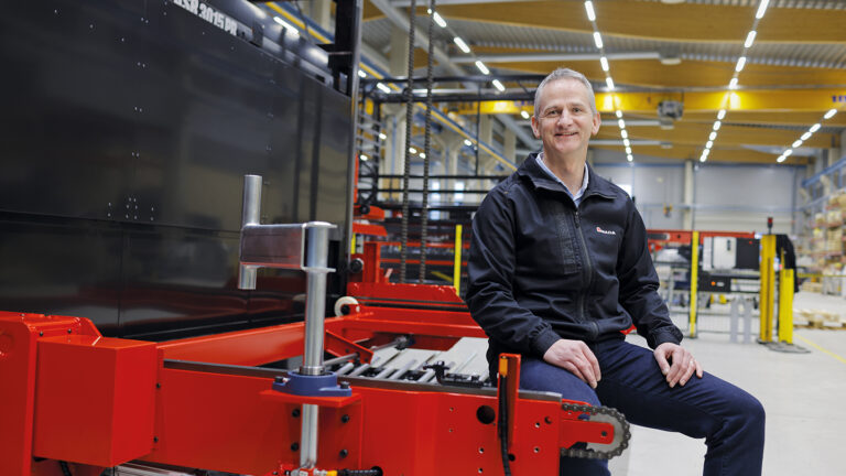 AMADA Automation Europe's CEO Greg Seymour sitting on a machine at the company's factory.