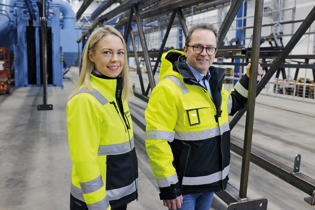 Best-Hall's Project Director Hanna Pahkala and Sales Director Leif Fagernäs pictured in a hall. Machinery in the background.