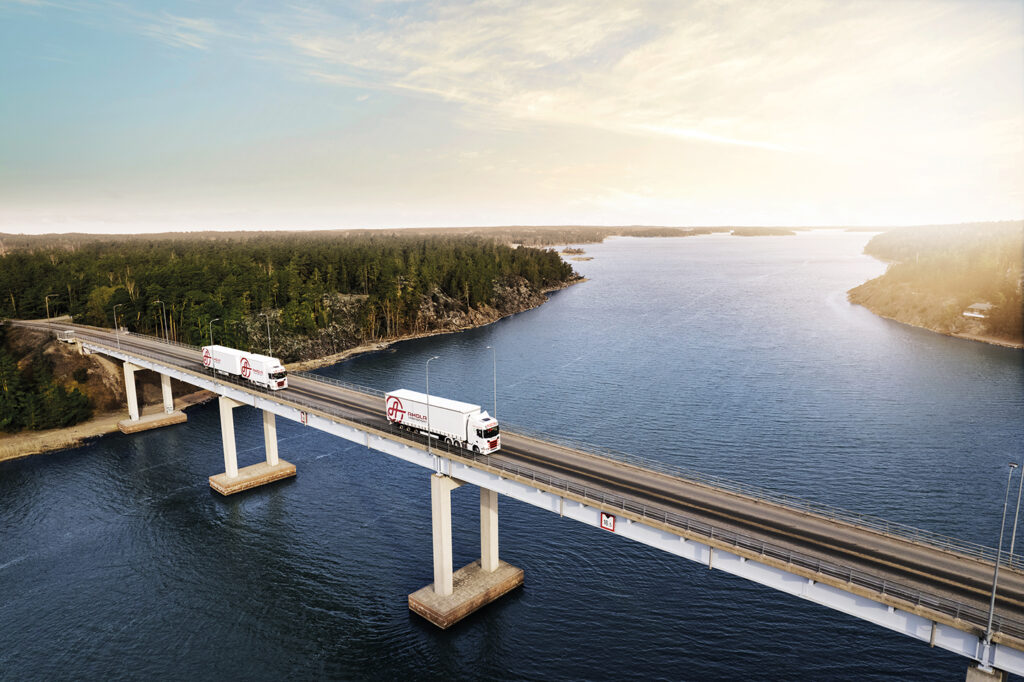 Two Ahola trucks driving across a bridge at sunrise.