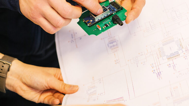 Two people examining a printed circuit board and looking at instructions.