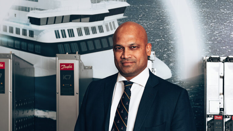 Shekhar Kubal, Danfoss' Global Head of Marine and Electrification pictured in front of Danfoss products and a picture of the passenger vessel Aurora Botnia.