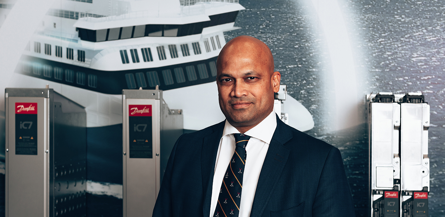 Shekhar Kubal, Danfoss' Global Head of Marine and Electrification pictured in front of Danfoss products and a picture of the passenger vessel Aurora Botnia.