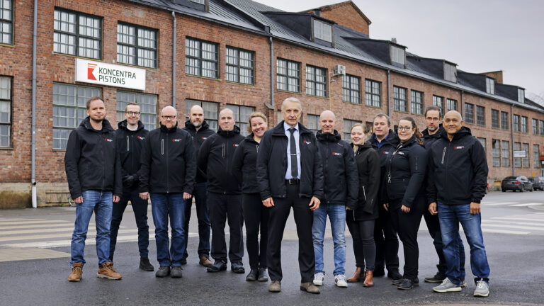 A group photo of Koncentra Pistons’ employees with CEO Sakari Pisilä in the middle. The company’s office building is in the background.