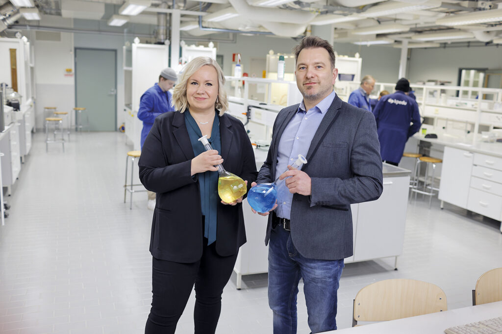 Osuvakoulutus' CEO Anu Haapasalo and Kpedu's Industry and Logistics Division Manager Petri Ahoniemi in a laboratory. Both are holding flat-bottomed flasks.