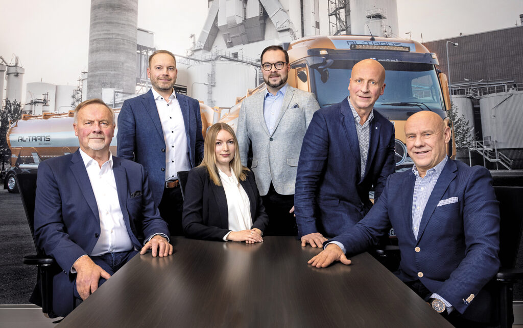 RL Trans’ Market Manager Andreas Lindedahl and ICT Manager Mathias Lindedahl pictured with four other employees. There is a big picture of a truck in the background.