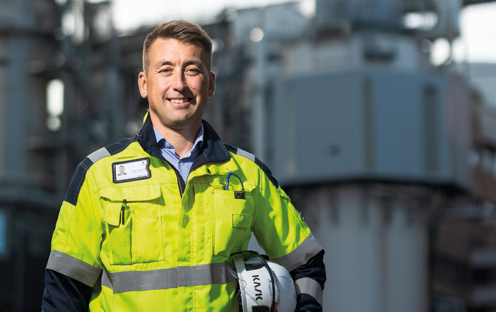 Simon Fagerudd, General Manager at the UPM pulp factory in Jakobstad. He is wearing protective clothing and holding a helmet. Factory in the background.