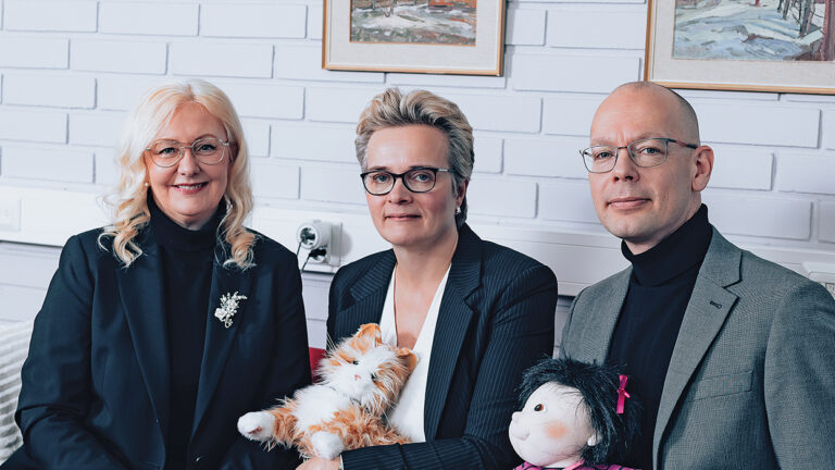 Vamia’s Principal Åsa Stenbacka, Welfare Services Lecturer Magdalena Vähäkangas, and Head of Division Toni Boren. Vähäkangas is holding a robotic therapy cat and Boren a therapy doll.