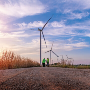 Employees wearing protective workwear and helmets walking by wind turbines.