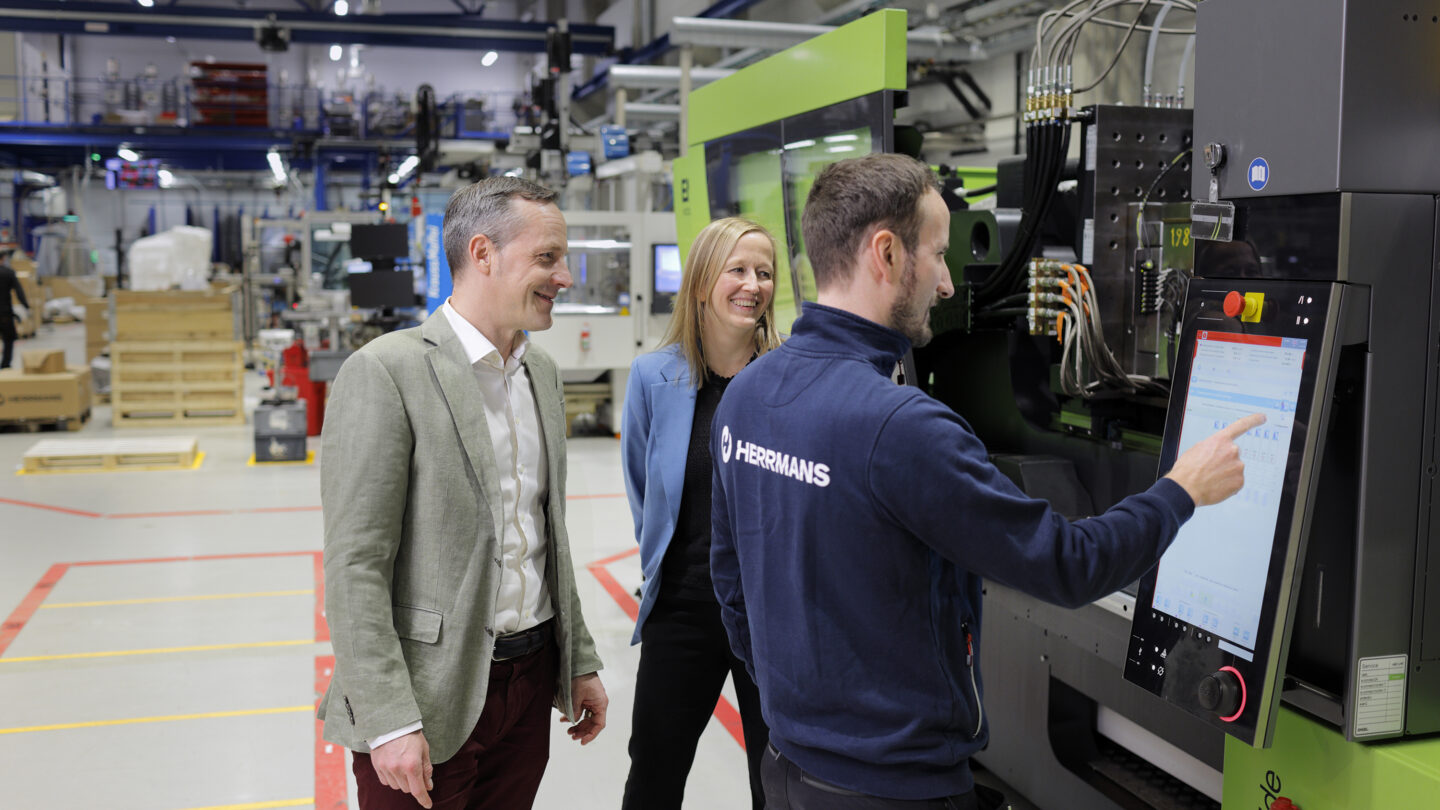 Dan Liljeqvist and Charlotte Sandström watching as Patrik Snellman uses a machine's touchscreen.