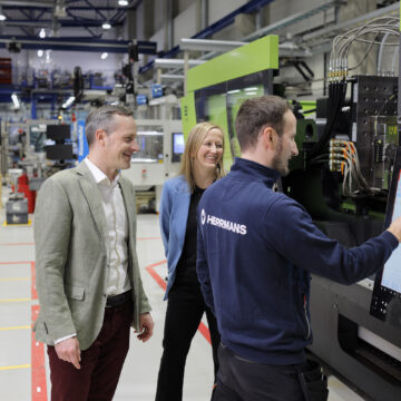 Dan Liljeqvist and Charlotte Sandström watching as Patrik Snellman uses a machine's touchscreen.